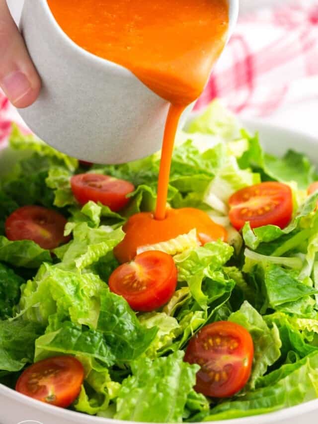 Pouring Catalina dressing over a simple salad of leafy greens and cherry tomatoes