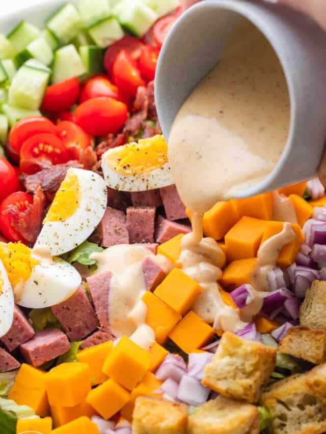 a cup of dressing being poured over a chefs salad