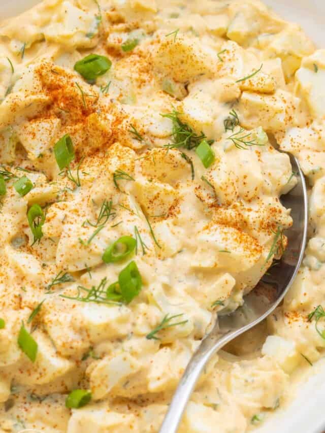 Closeup of a bowl of homemade egg salad garnished with paprika, dill, and green onion.
