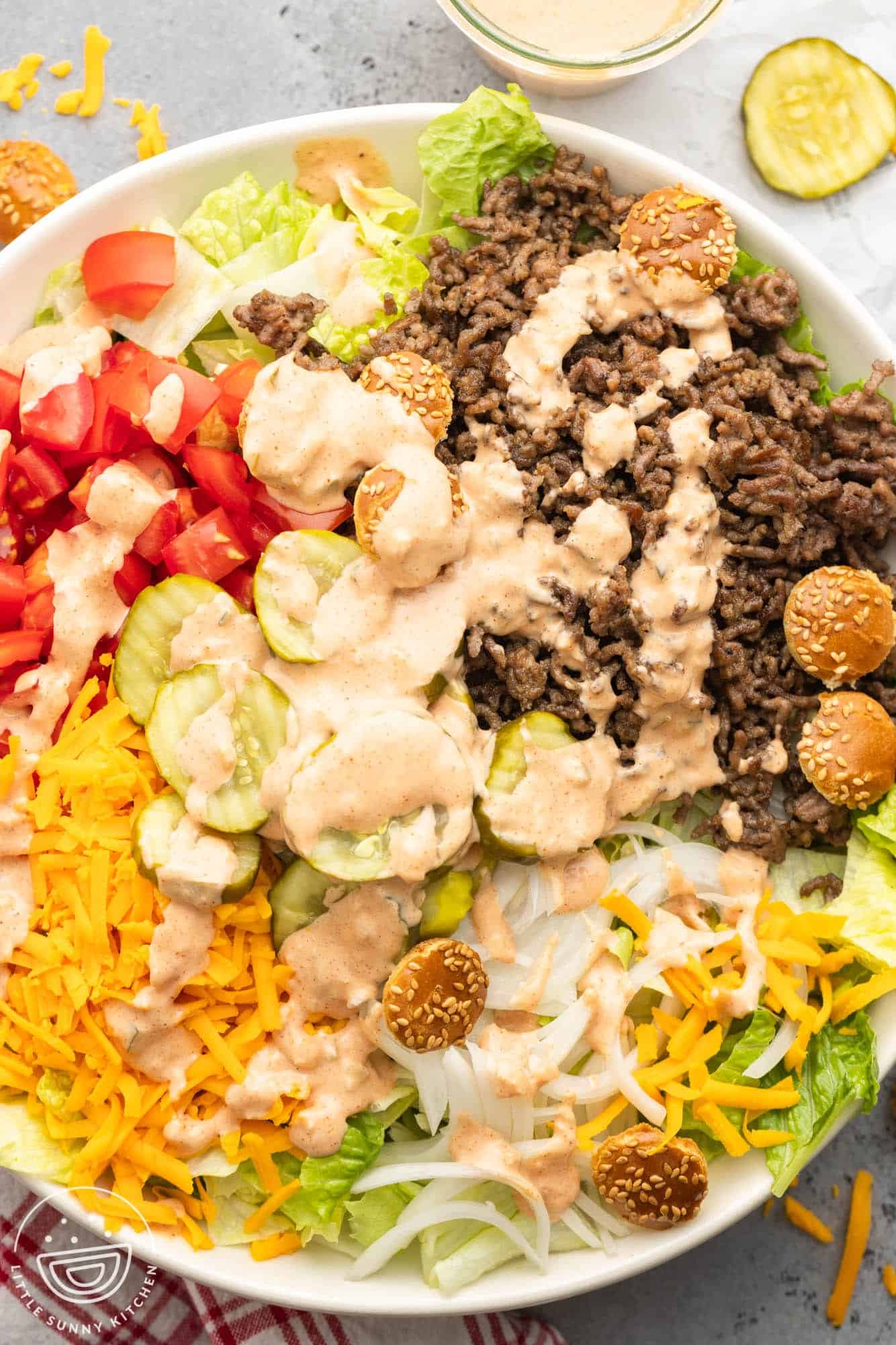 a large salad topped with beef, cheese, tomatoes, big mac sauce, and pickles.