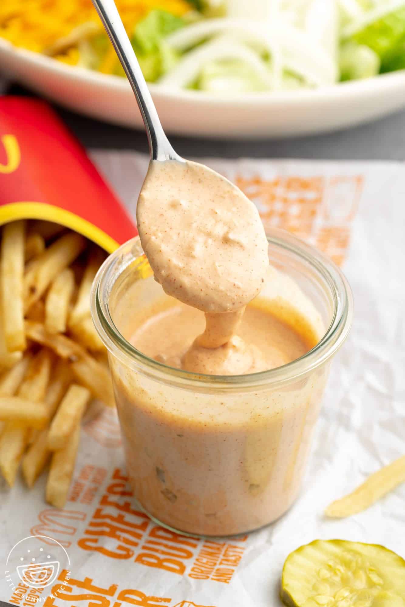 Copycat Big Mac sauce in a jar with a spoon, with fries and a salad in the background