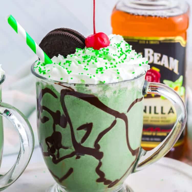 Boozy Oreo Shamrock Shake in a glass mug, topped with whipped cream, a cherry, and sprinkles.