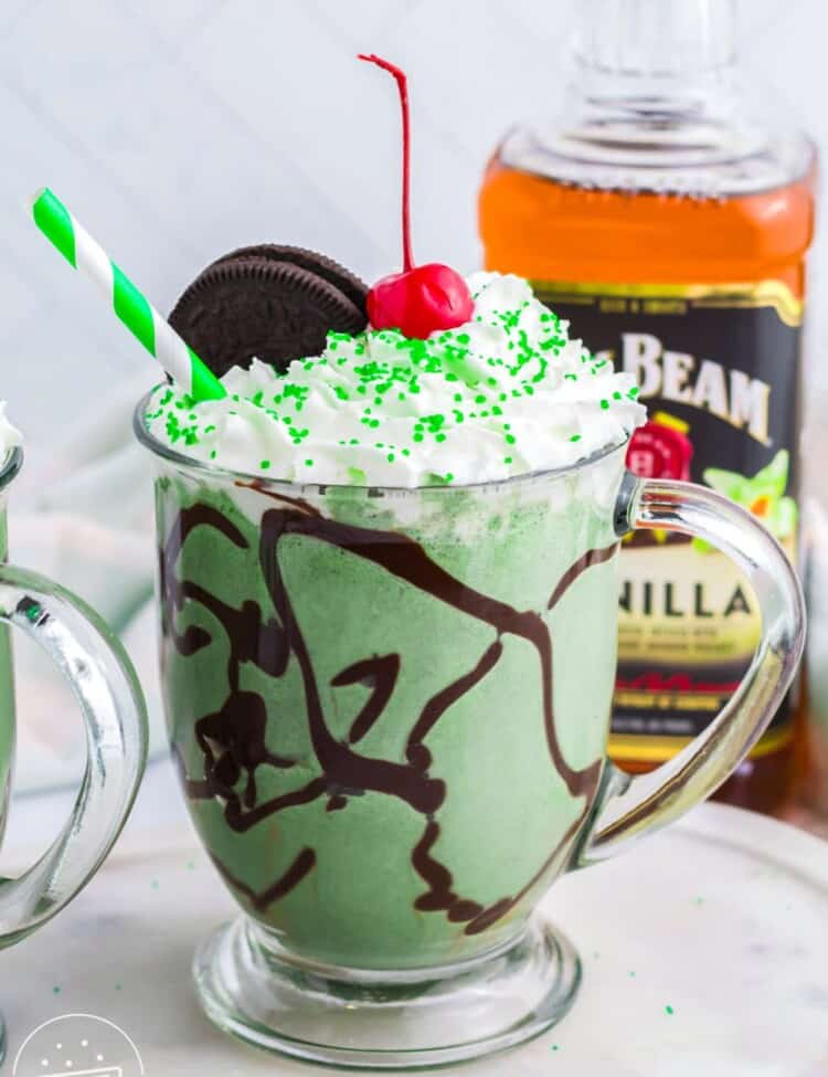 Boozy Oreo Shamrock Shake in a glass mug, topped with whipped cream, a cherry, and sprinkles.