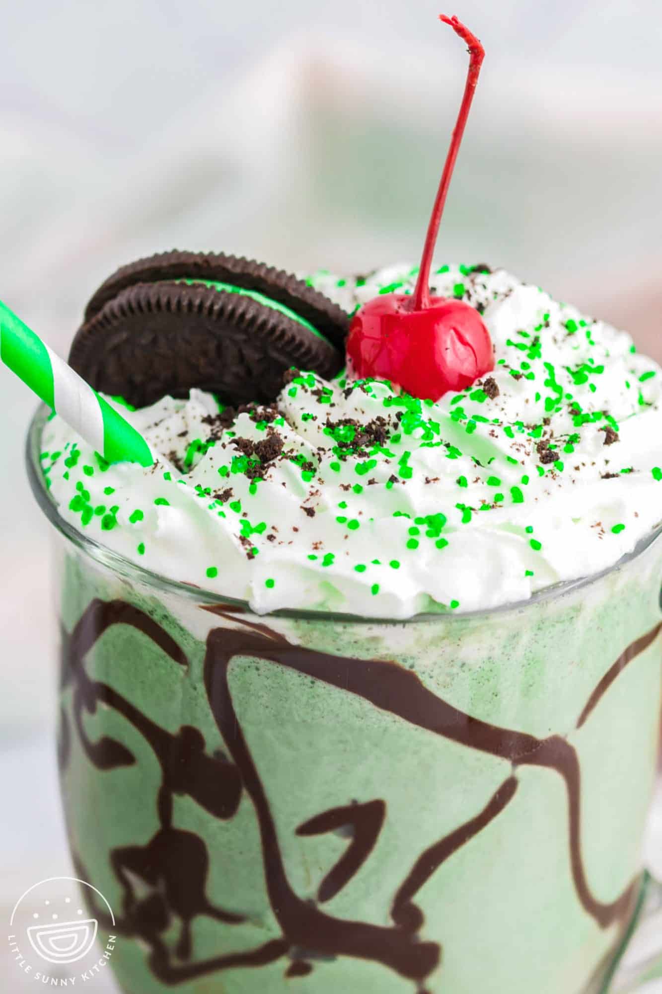 Close up shot of shamrock shake topped with whipped cream, mint oreo, and a cherry
