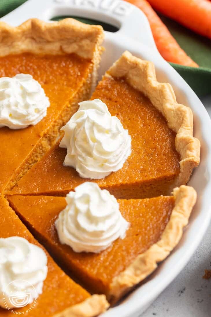 A pumpkin pie with a golden crust is sliced and topped with swirls of whipped cream—a perfect choice for National Pie Day or anyone searching for easy pie recipes.