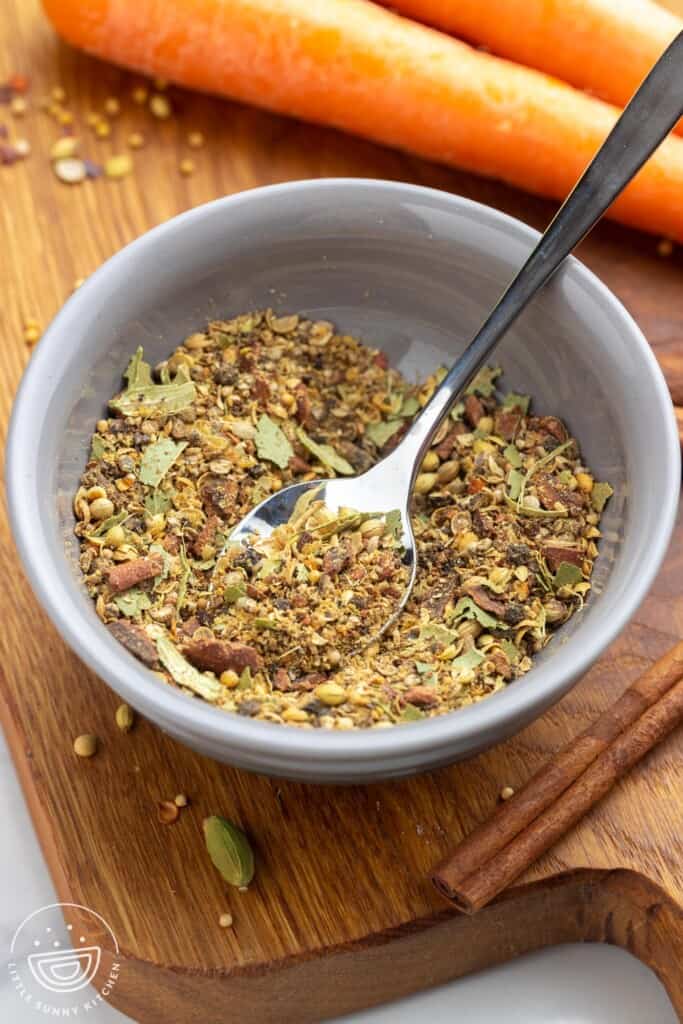 Corned beef seasoning in a gray bowl with a small spoon, and carrots in the background