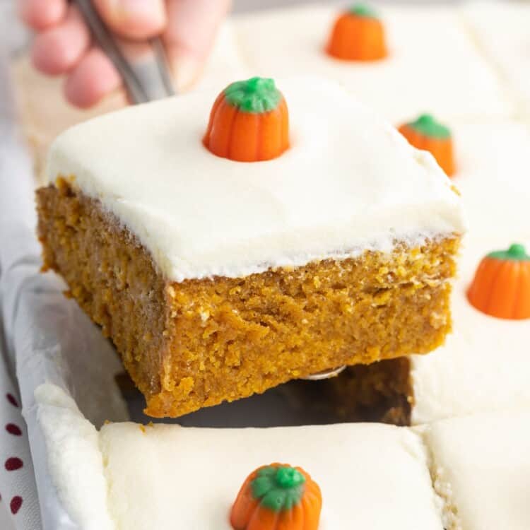 a slice of frosted pumpkin cake lifted out of the pan. Each square is topped with a candy pumpkin