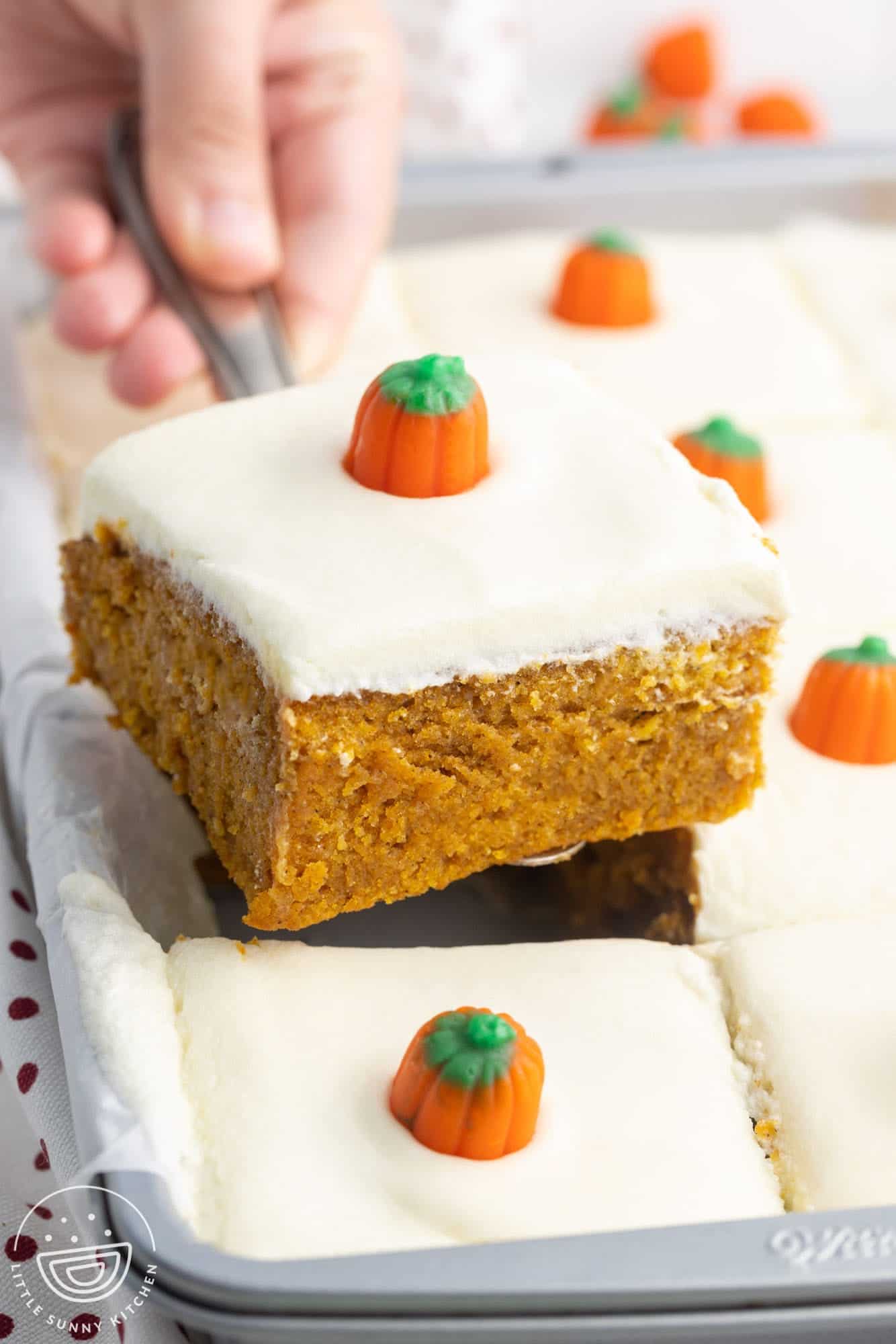 a slice of frosted pumpkin cake lifted out of the pan. Each square is topped with a candy pumpkin