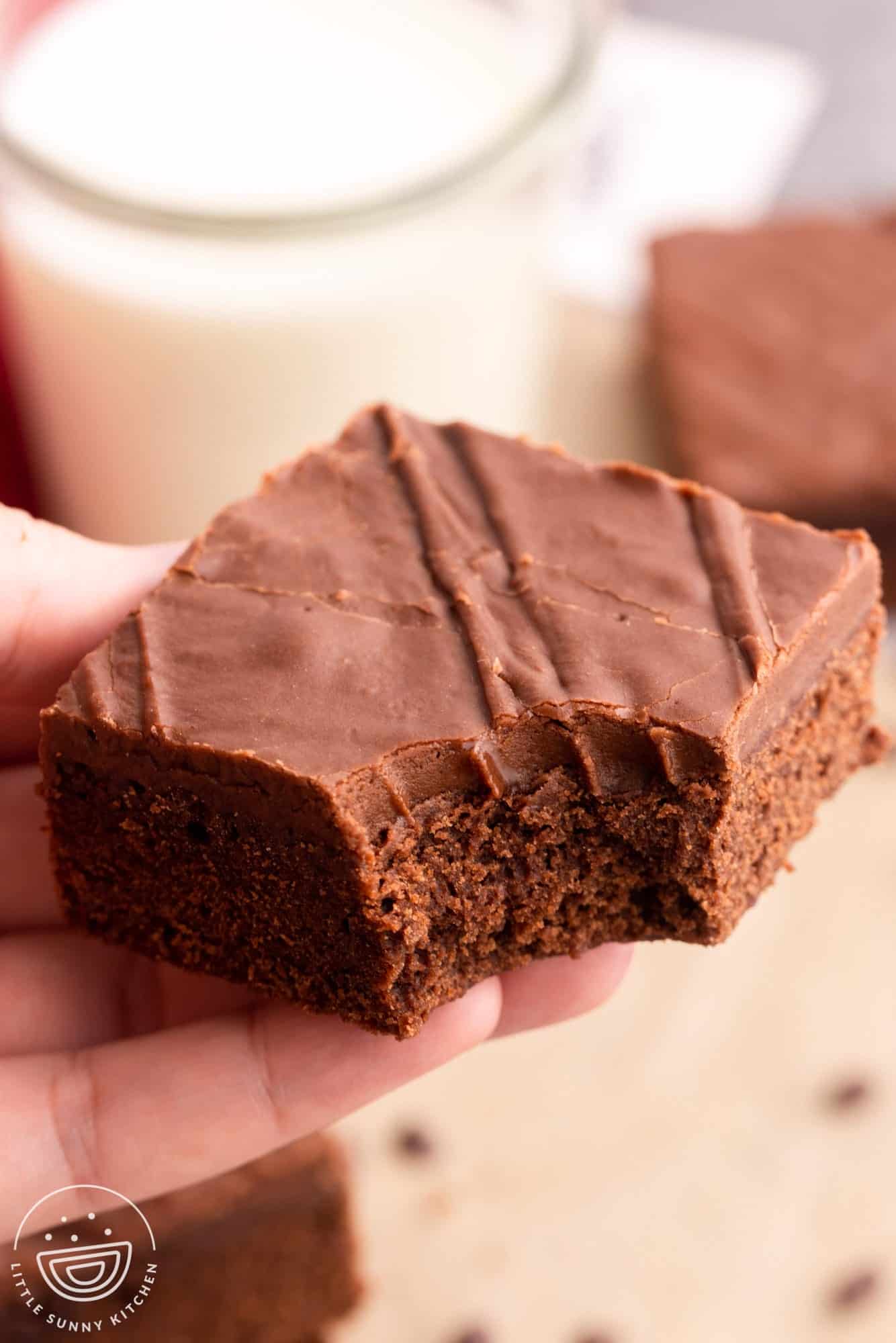 a hand holding a frosted brownie. A bite has been taken from the corner.