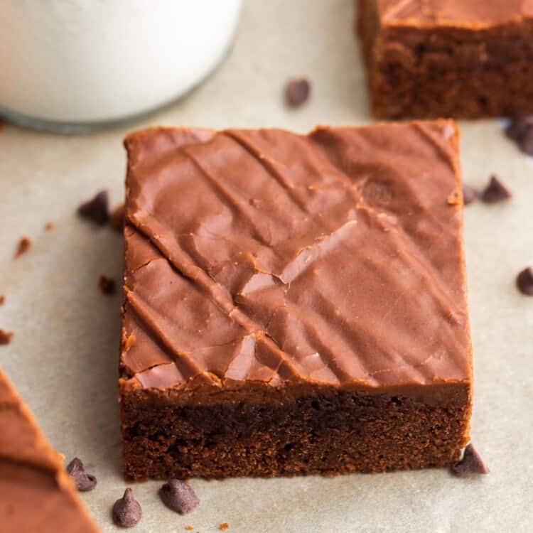 a square lunch lady brownie with frosting next to a glass of milk.