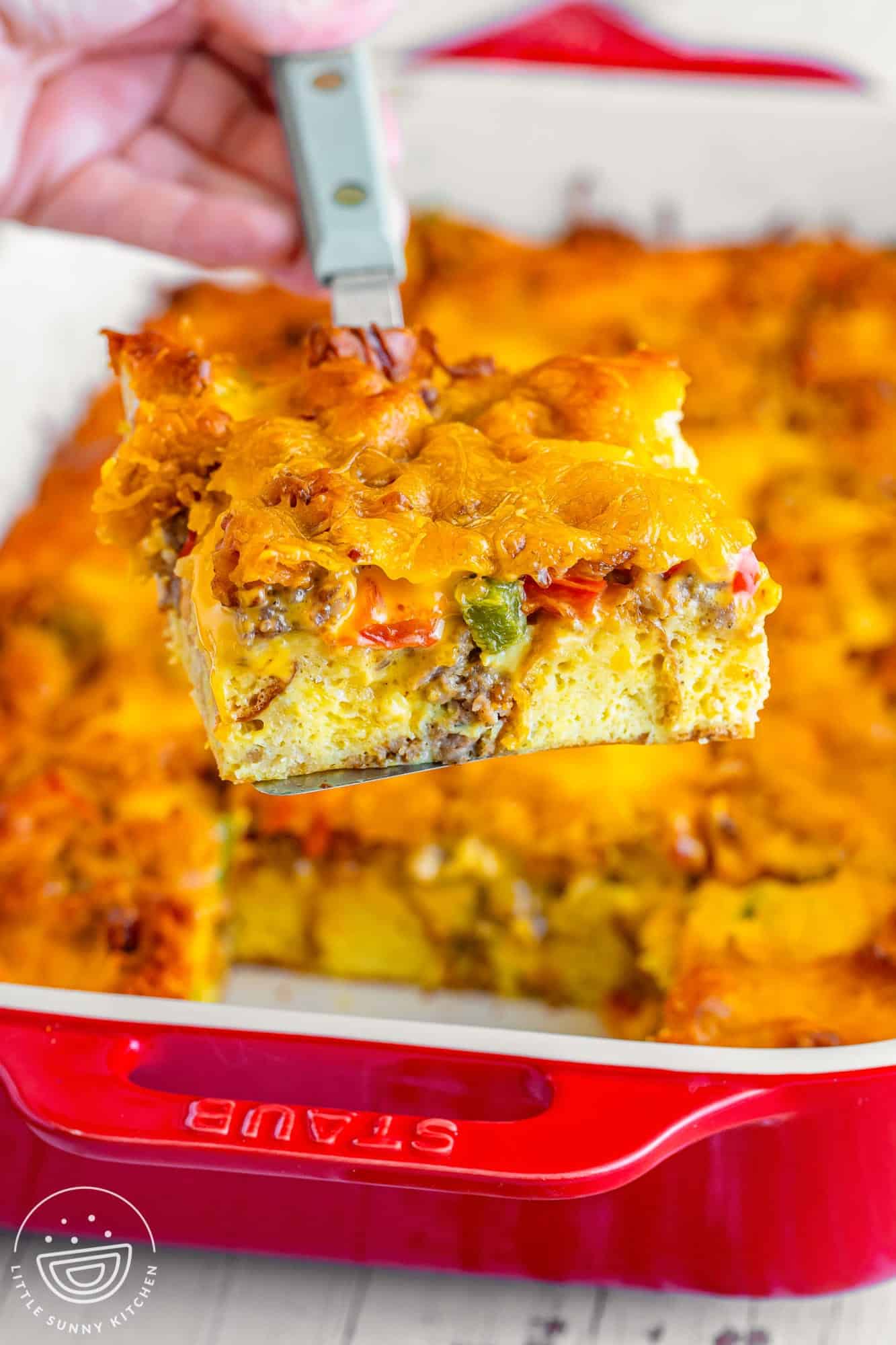 a piece of christmas breakfast casserole being lifted out of a red casserole dish.