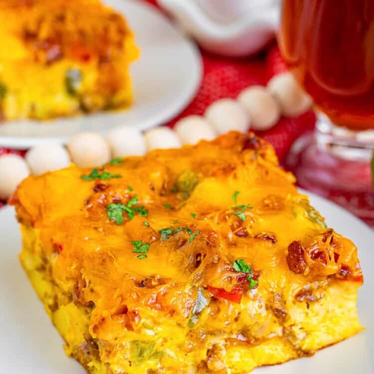 a square slice of overnight christmas breakfast casserole on a plate, sitting on a red tablecloth.