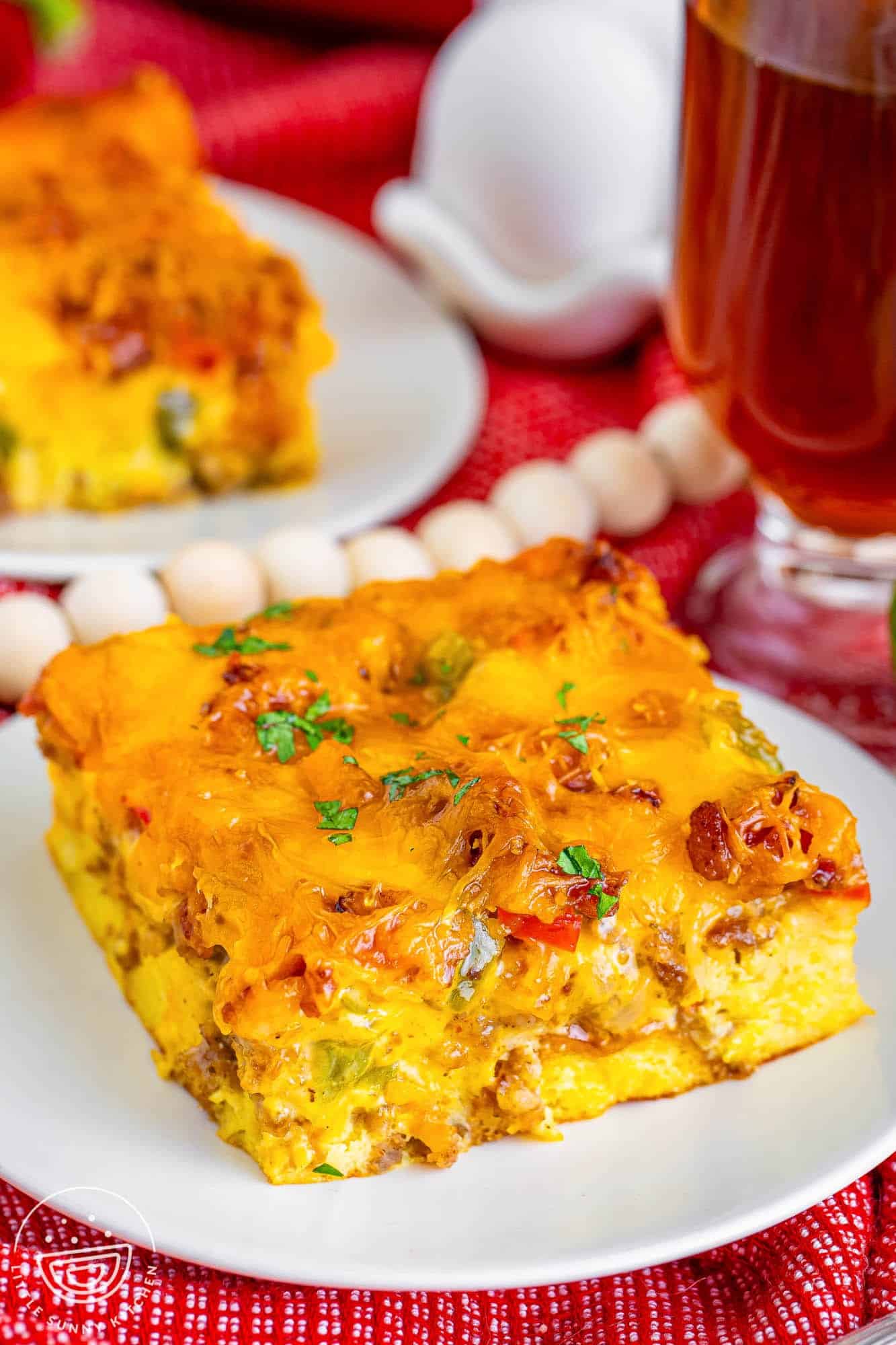 a square slice of overnight christmas breakfast casserole on a plate, sitting on a red tablecloth.