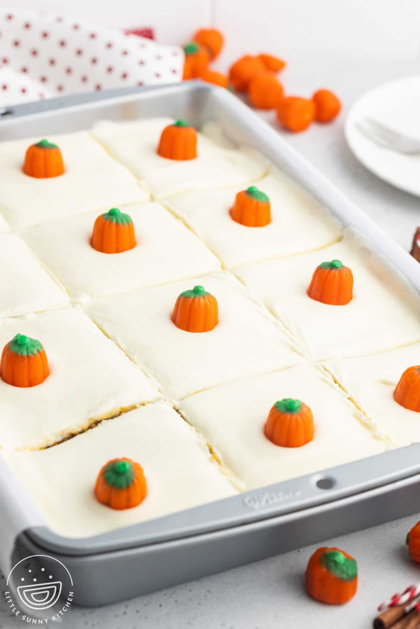 a 9x13 pan of cake, sliced into squares. The cake is frosted and each piece is topped with a candy corn pumpkin.