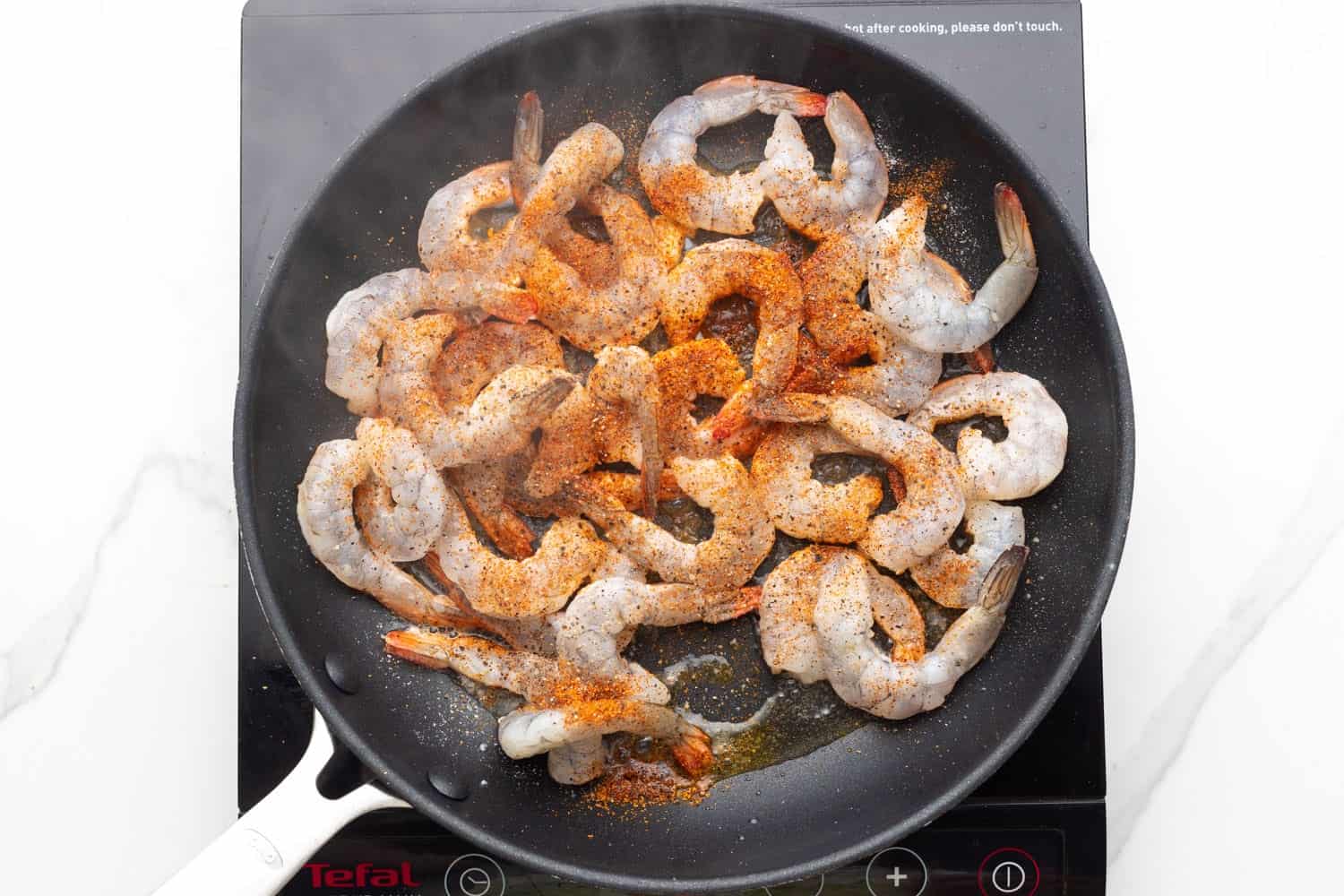 A non-stick frying han holding seasoned shrimp and oil.