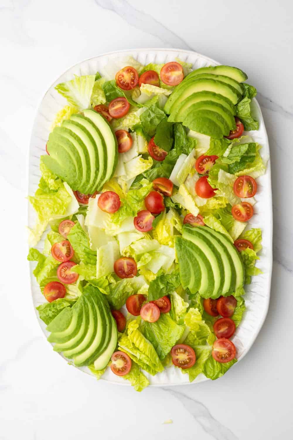 A platter of romaine lettuce, halved cherry tomatoes, and sliced avocado