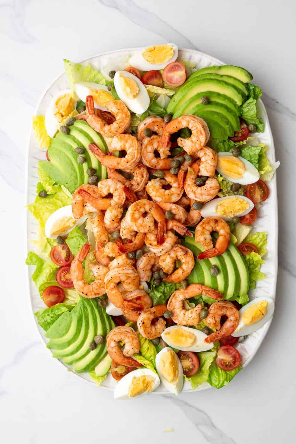 Hard boiled eggs and shrimp with capers on a salad.