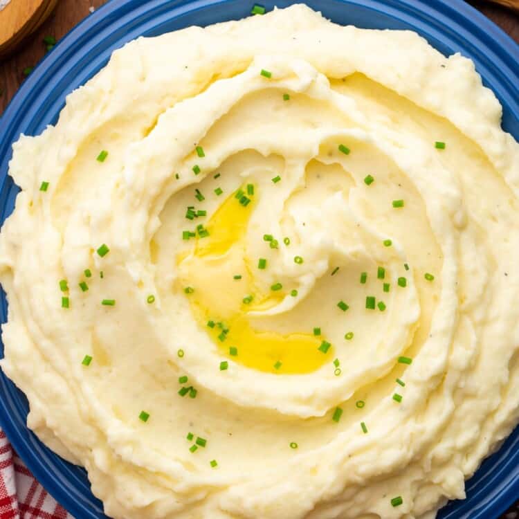 Overhead shot of creamy mashed potatoes served in a large bowl, garnished with sliced chives and melted butter