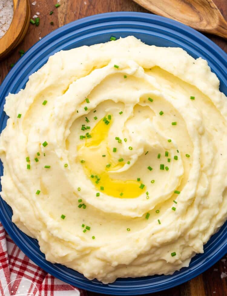 Overhead shot of creamy mashed potatoes served in a large bowl, garnished with sliced chives and melted butter