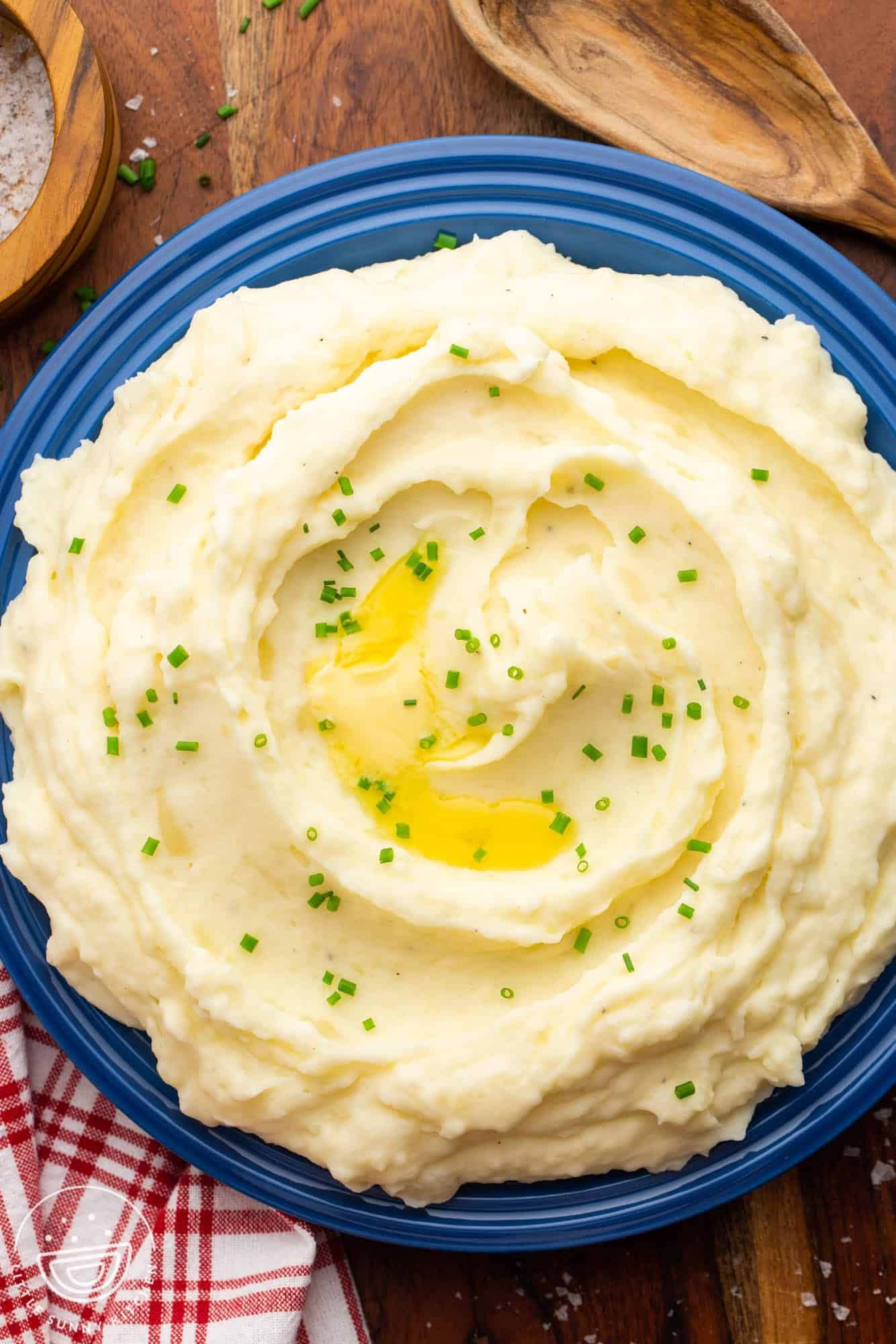 Overhead shot of creamy mashed potatoes served in a large bowl, garnished with sliced chives and melted butter