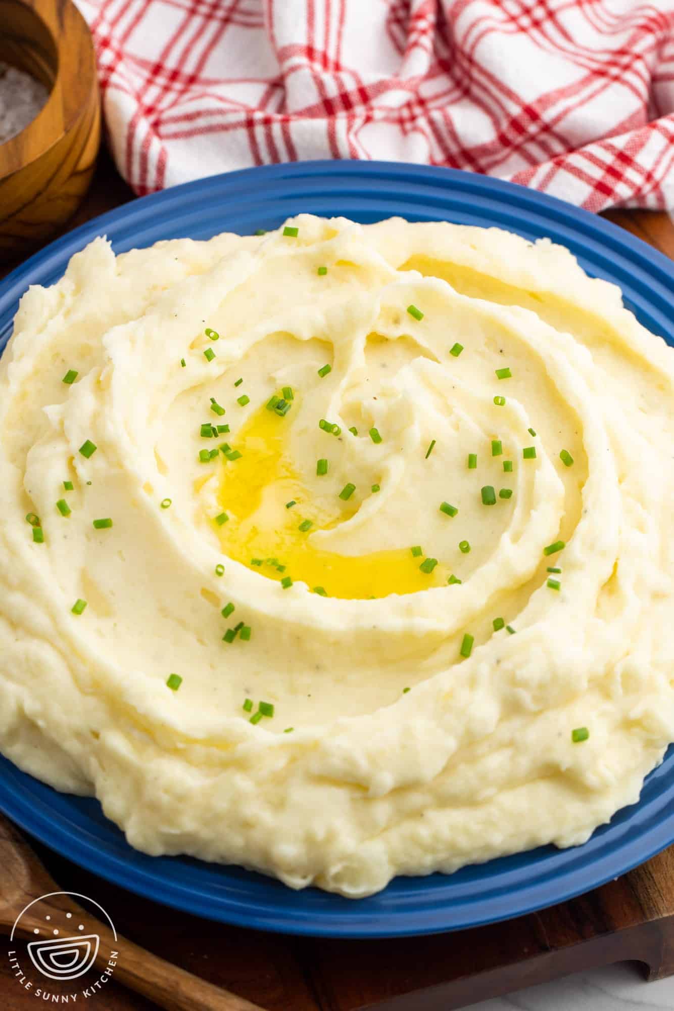 Angle shot of creamy mashed potatoes served in a blue bowl, garnished with sliced chives