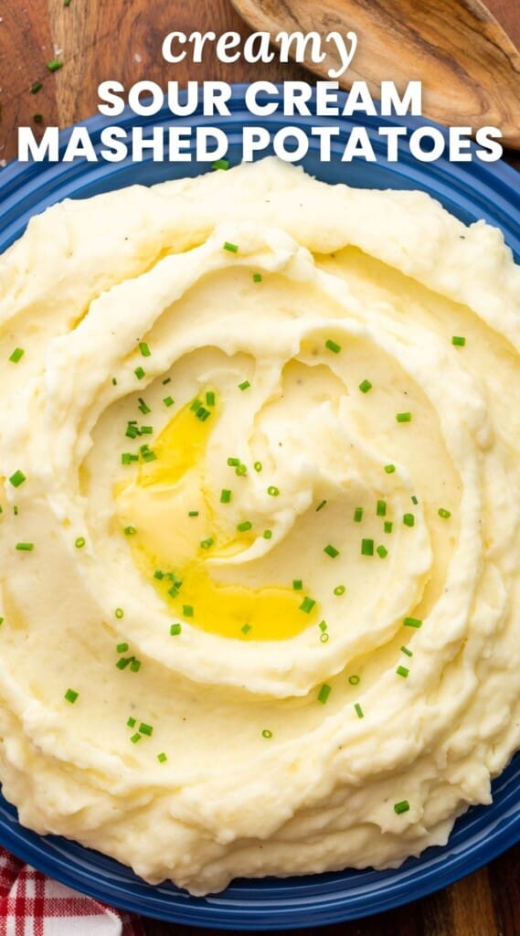 Overhead shot of creamy mashed potatoes served in a large bowl, garnished with sliced chives and melted butter. And overlay text that says "creamy sour cream mashed potatoes"