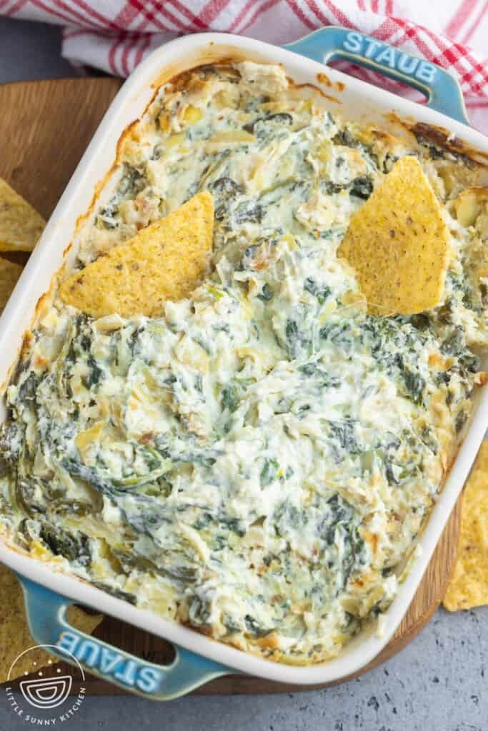 Overhead shot of baked spinach and artichoke dip in a rectangular small dish, and 2 tortilla chips.