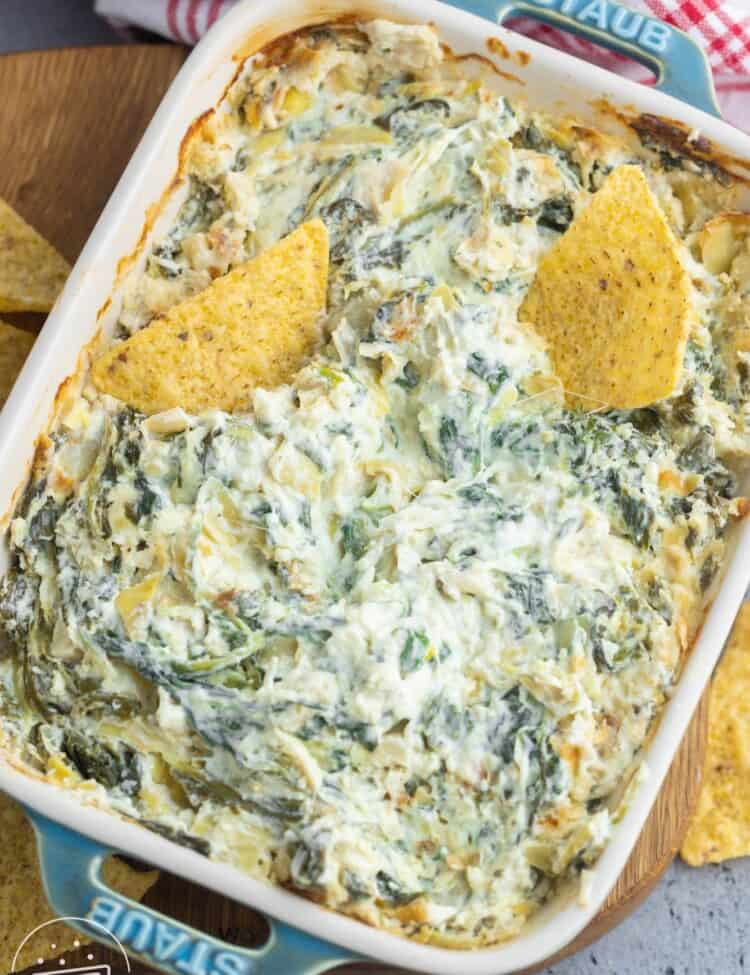 Overhead shot of baked spinach and artichoke dip in a rectangular small dish, and 2 tortilla chips.