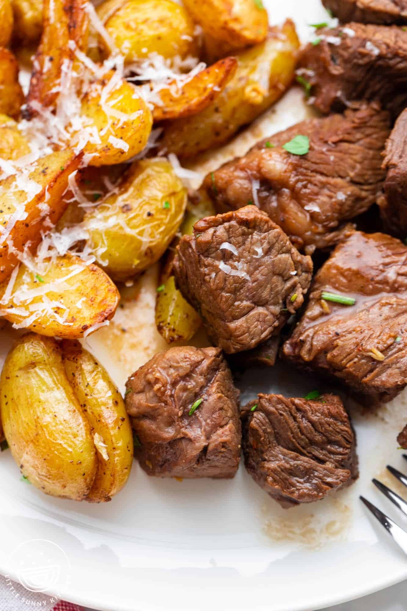 steak bites and potatoes with parmesan cheese on a dinner plate.
