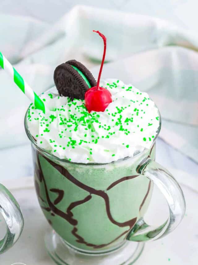 Boozy Oreo Shamrock Shake in a glass mug, topped with whipped cream, a cherry, and sprinkles.