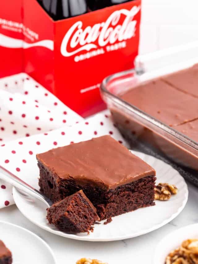 a dessert plate with a slice of chocolate cake. A fork has removed a bite from the corder. A box of coca cola is in the background