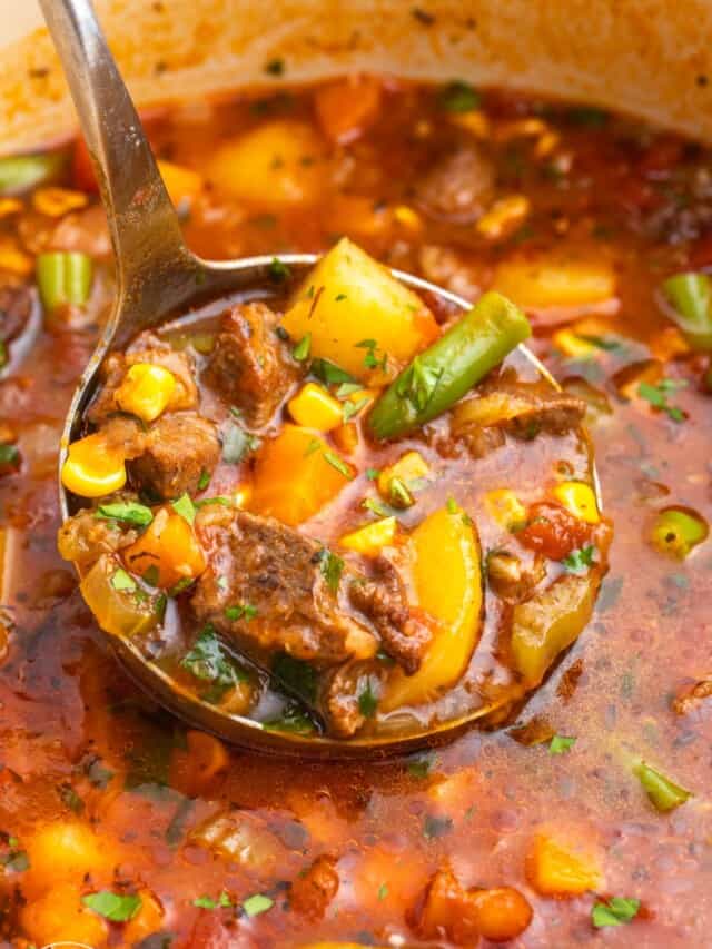 beef vegetable soup in a pot. a ladle is holding some of it up.