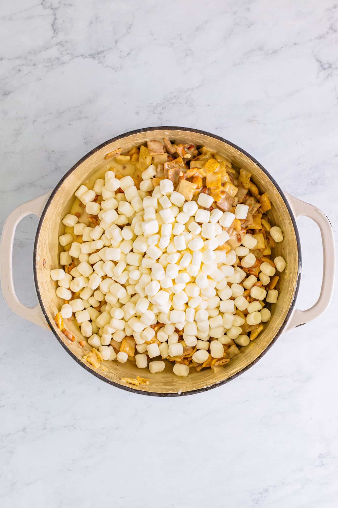 Mini marshmallows, chex, pretzels, and nuts added to a pot of melted butter and marshmallows to make chex mix treats.