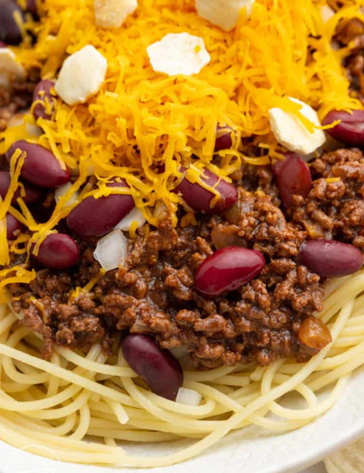 a plate of spaghetti with cincinnati chili, topped with cheese and crackers.