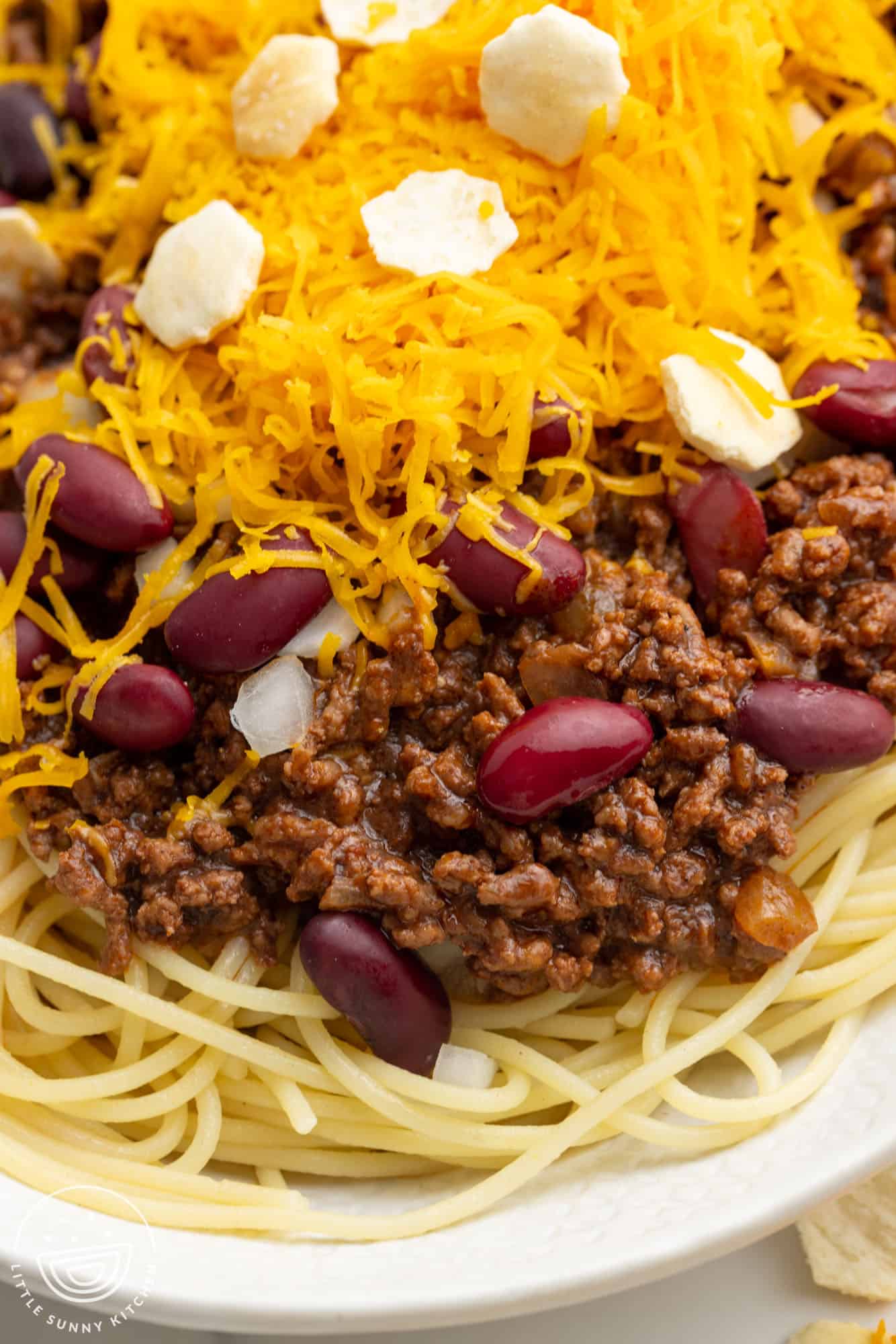 a plate of spaghetti with cincinnati chili, topped with cheese and crackers.