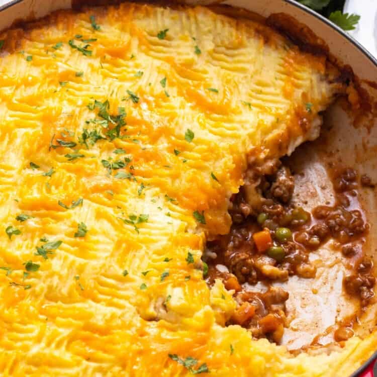 a red, round baking dish filled with cottage meat pie topped with cheesy mashed potatoes.