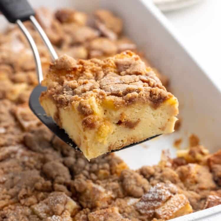 a square of french toast casserole lifted out of the pan, with a creamy interior and crumbly topping.