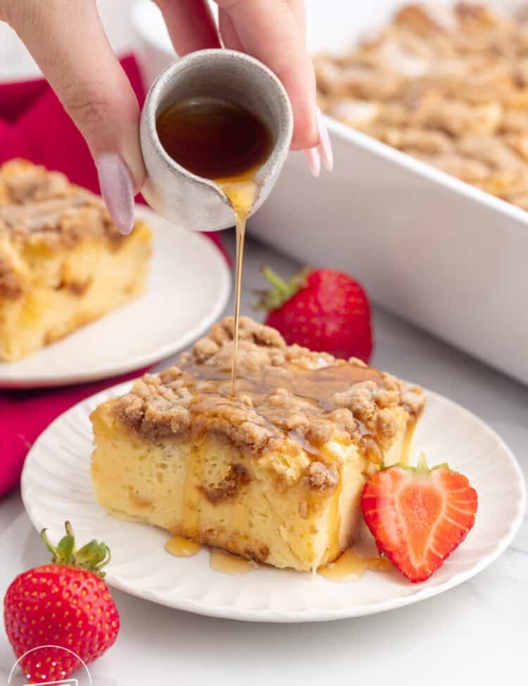 a hand pouring maple syrup over a slice of french toast casserole.