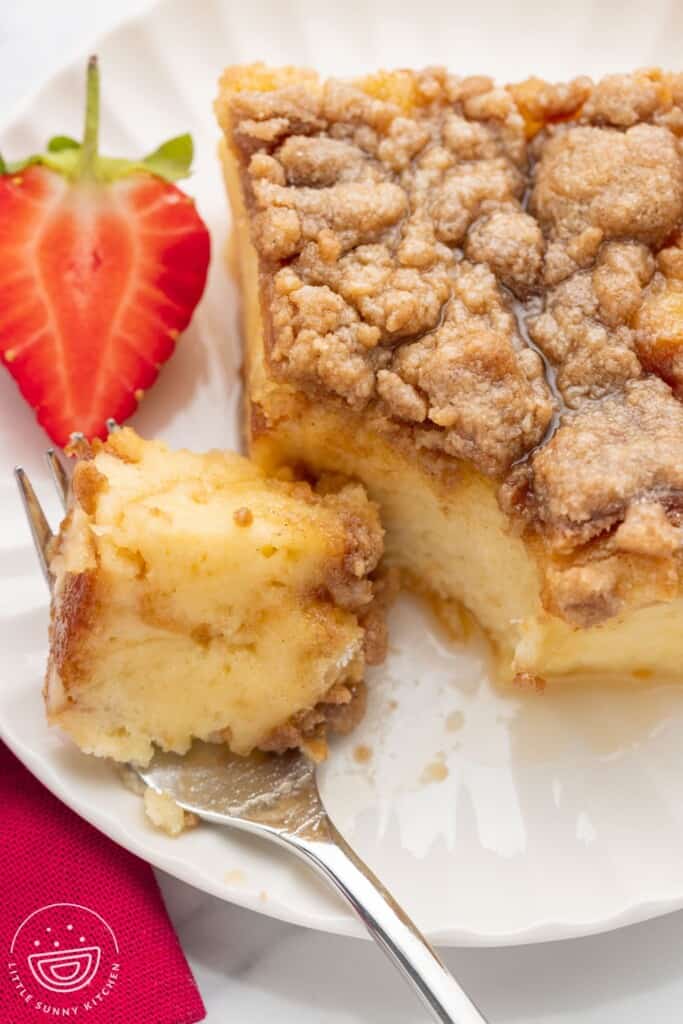 a square piece of fresh toast casserole on a plate with a strawberry garnish. A fork is holding a bite.