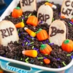 Graveyard chocolate cheesecake dip in a small rectangular dish, with milano cookies, candy corn, pumpkin candy and sprinkles.