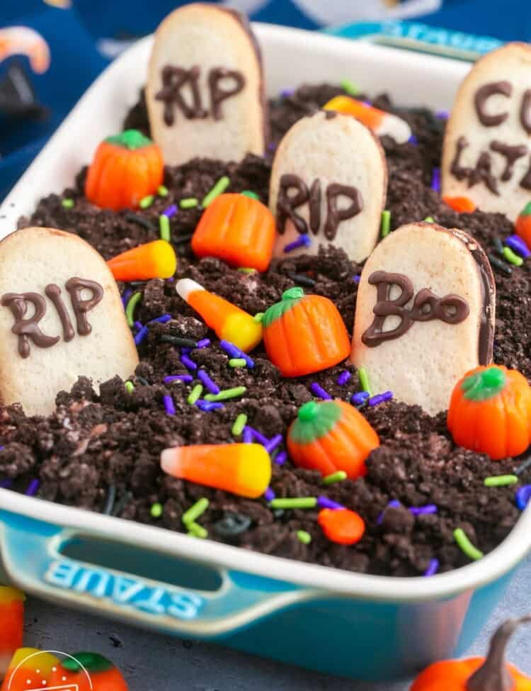 Graveyard chocolate cheesecake dip in a small rectangular dish, with milano cookies, candy corn, pumpkin candy and sprinkles.