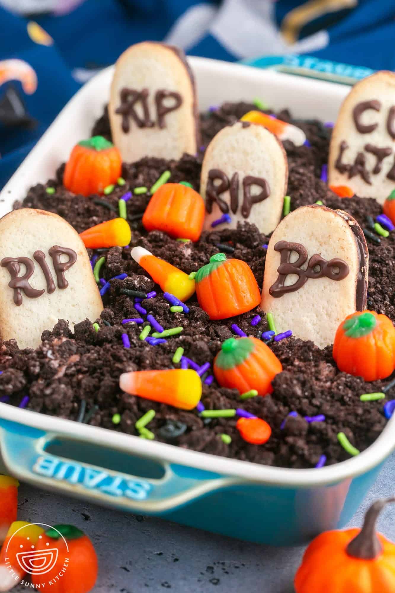Graveyard chocolate cheesecake dip in a small rectangular dish, with milano cookies, candy corn, pumpkin candy and sprinkles.
