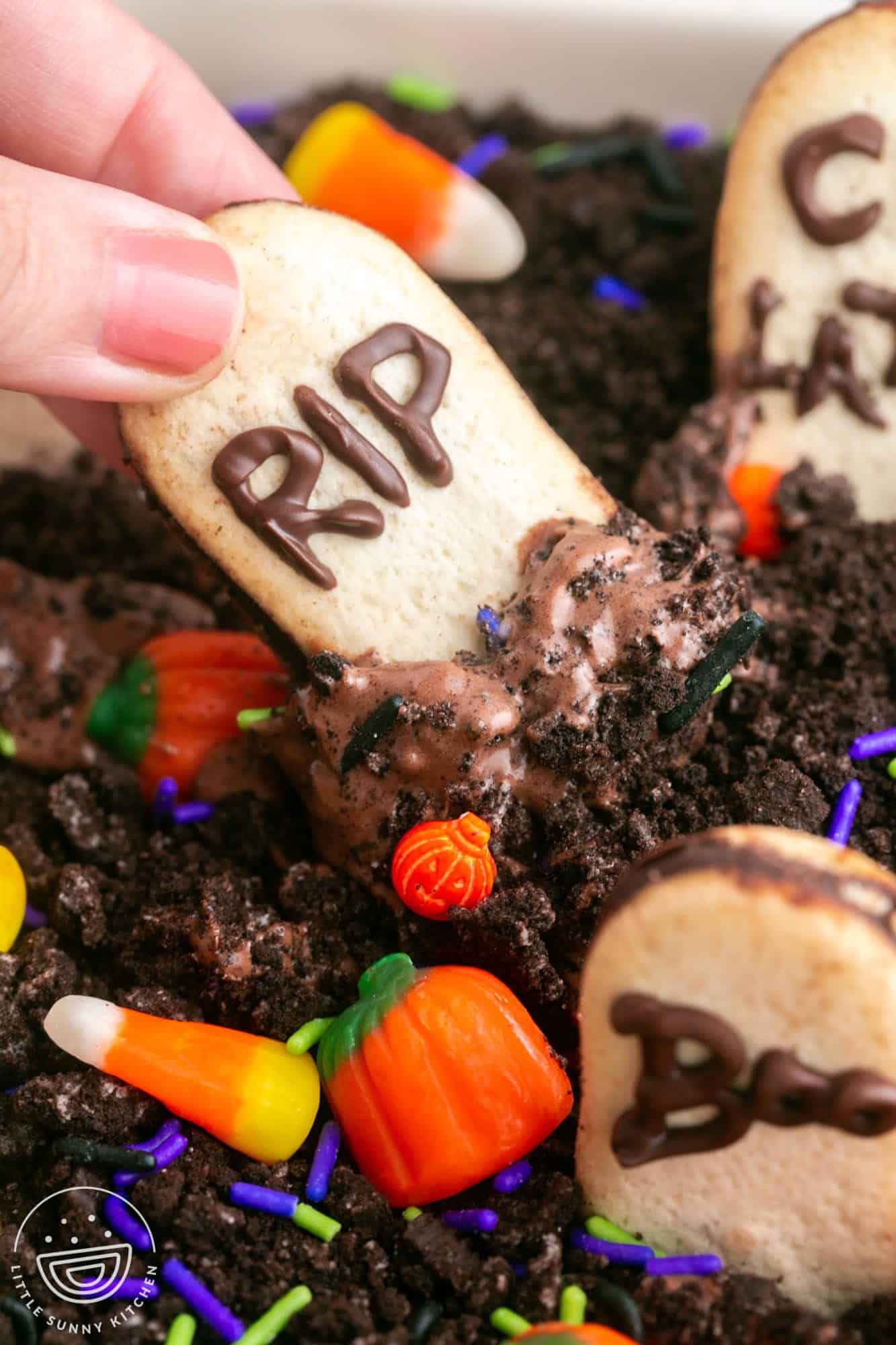 Dipping a milano cookie in chocolate cheesecake dip decorated with halloween themed candy and sprinkles