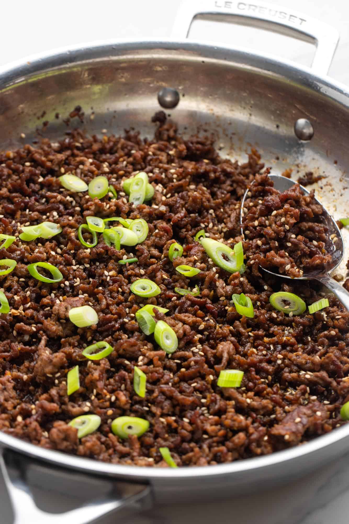 korean beef in a skillet, topped with sesame seeds and sliced green onion