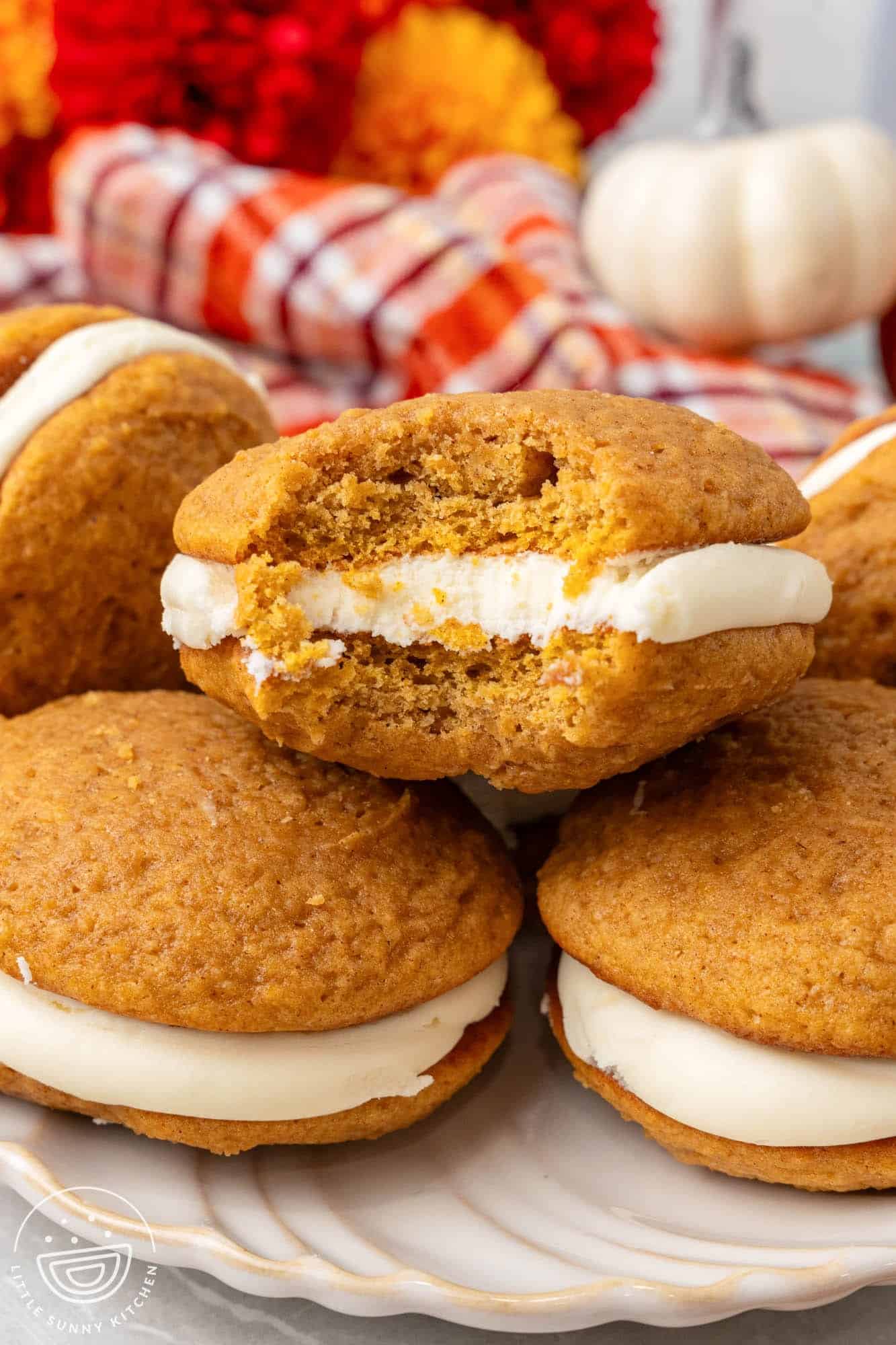 pumpkin whoopie pies on a plate. One has been bitten into to show fluffy interior texture.