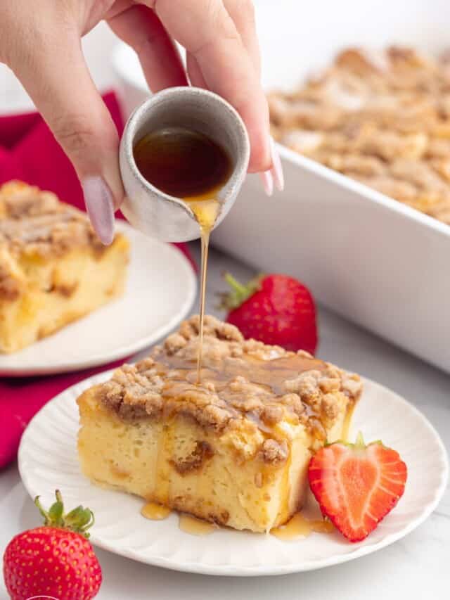 a hand pouring maple syrup over a slice of french toast casserole.