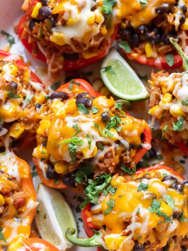 vegetarian stuffed peppers with beans, corn, and cheese, garnished with fresh herbs and lime wedges