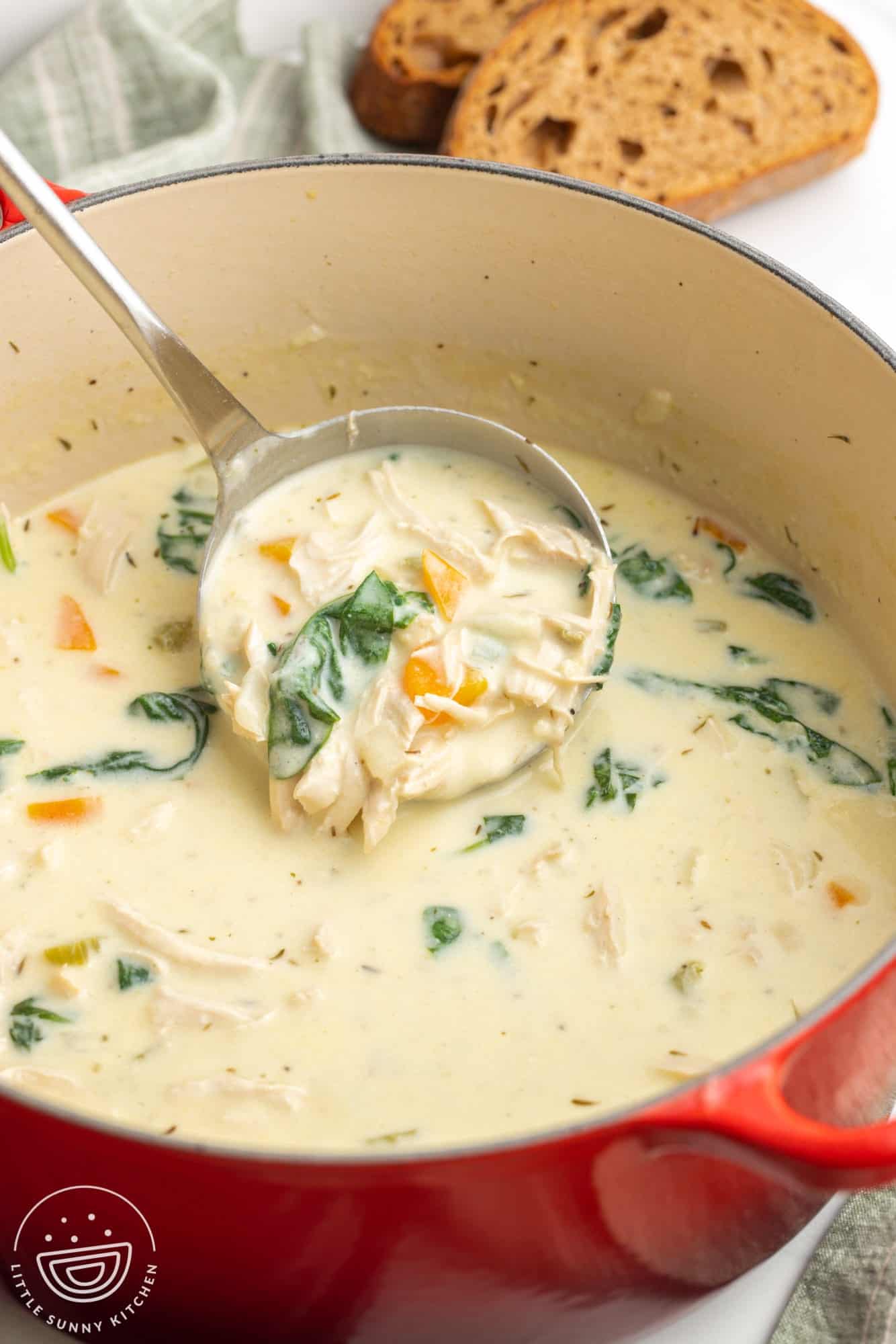 a pot of chicken florentine soup. A ladle is lifting up a serving filled with shredded chicken, carrots, and spinach.