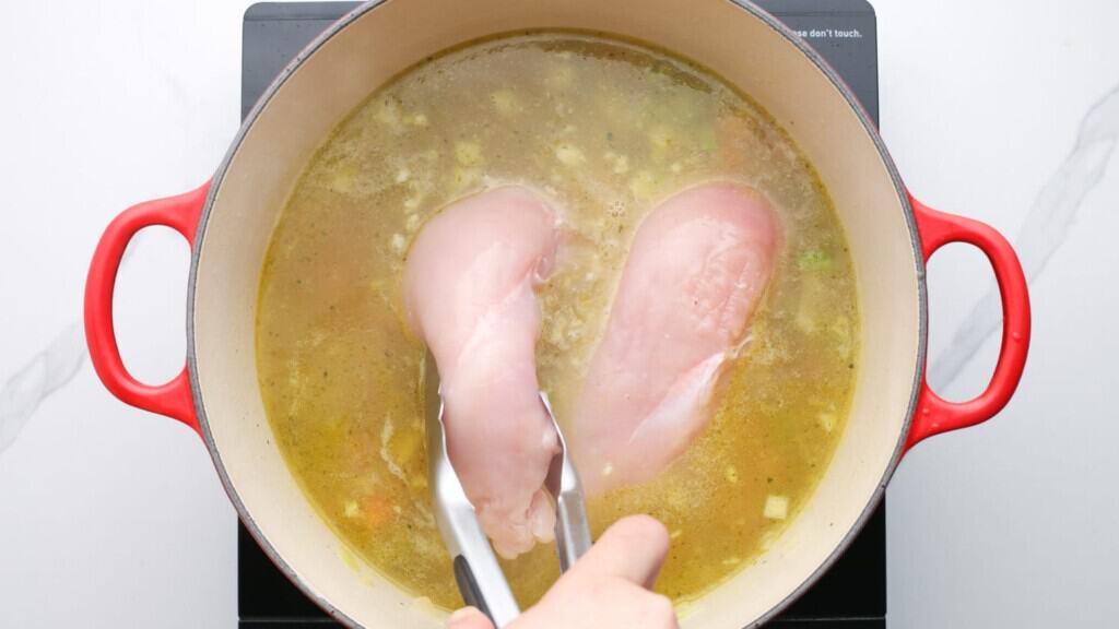 chicken breasts added to soup with tongs.