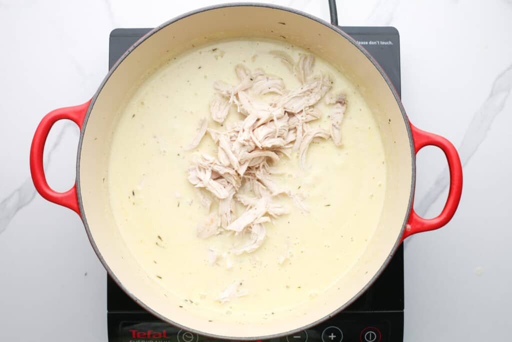 shredded chicken added to a pot of creamy soup
